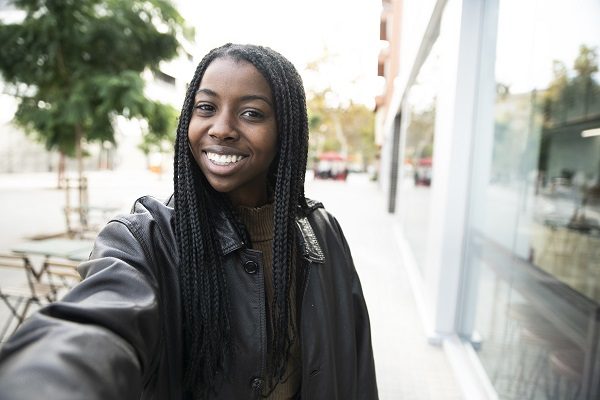 happy young woman smiling taking a selfie portrait in the city - portrait of young afro american woman taking a selfie outdoor. High quality photo